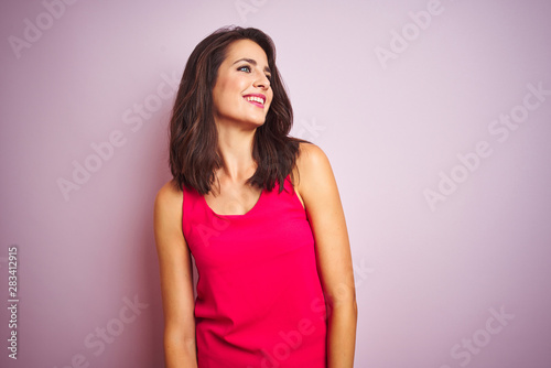 Young beautiful woman wearing t-shirt standing over pink isolated background looking away to side with smile on face  natural expression. Laughing confident.