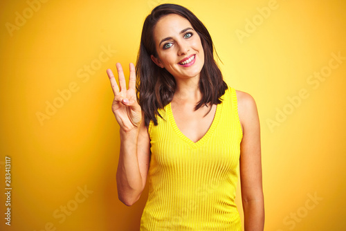 Young beautiful woman wearing t-shirt standing over yellow isolated background showing and pointing up with fingers number three while smiling confident and happy.