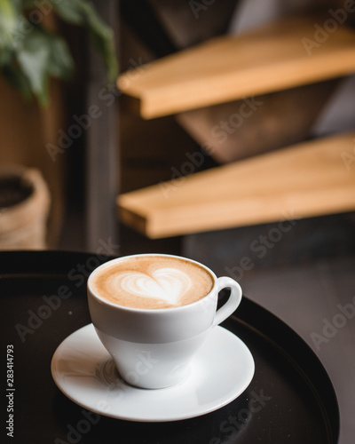 One cup of cappuccino with latte art on black table, white ceramic cup, top view. Cafe culture.