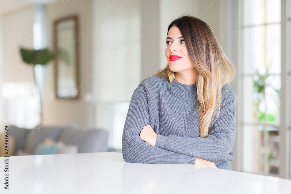 Young beautiful woman wearing winter sweater at home smiling looking side and staring away thinking. Young beautiful woman wearing winter sweater at home smiling looking side and staring away thinking.