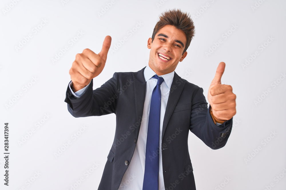 Young handsome businessman wearing suit standing over isolated white background approving doing positive gesture with hand, thumbs up smiling and happy for success. Winner gesture. Young handsome businessman wearing suit standing over isolated white background approving doing positive gesture with hand, thumbs up smiling and happy for success. Winner gesture.