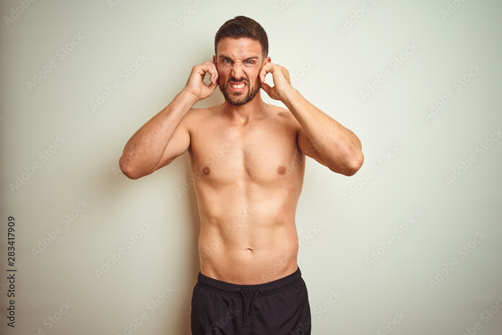 Fototapeta premium Young handsome shirtless man over isolated background covering ears with fingers with annoyed expression for the noise of loud music. Deaf concept.