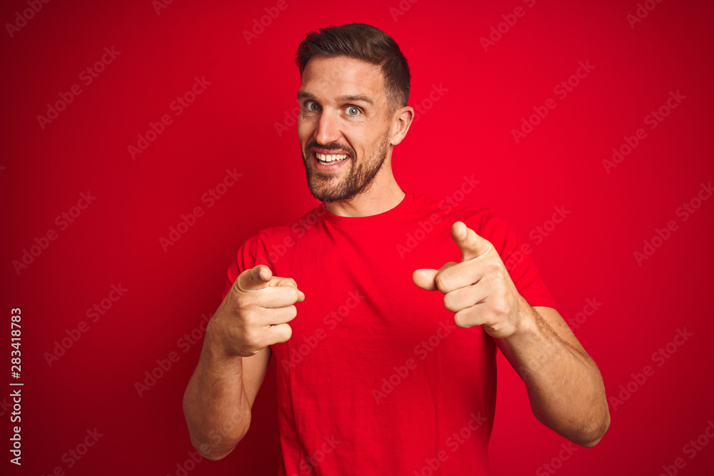 Young handsome man wearing casual t-shirt over red isolated background pointing fingers to camera with happy and funny face. Good energy and vibes. Young handsome man wearing casual t-shirt over red isolated background pointing fingers to camera with happy and funny face. Good energy and vibes.