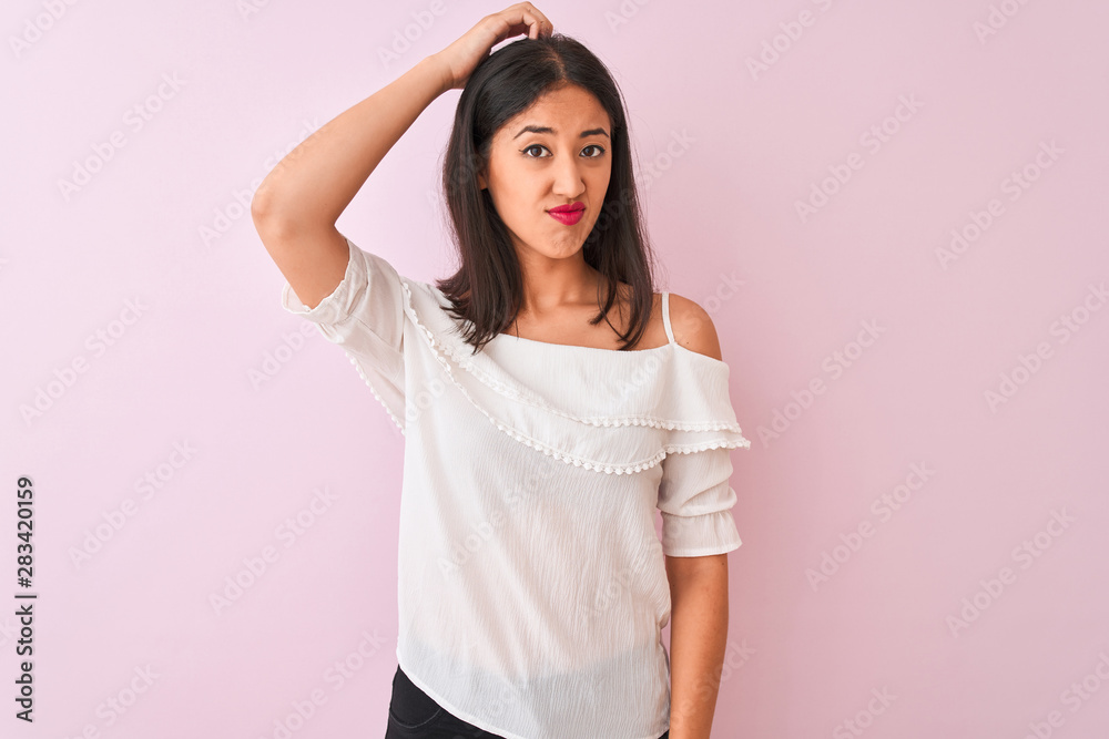 Beautiful chinese woman wearing white t-shirt standing over isolated pink background confuse and wonder about question. Uncertain with doubt, thinking with hand on head. Pensive concept. Beautiful chinese woman wearing white t-shirt standing over isolated pink background confuse and wonder about question. Uncertain with doubt, thinking with hand on head. Pensive concept.