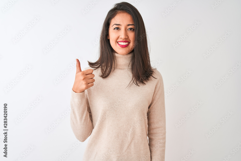Beautiful chinese woman wearing turtleneck sweater standing over isolated white background doing happy thumbs up gesture with hand. Approving expression looking at the camera showing success.