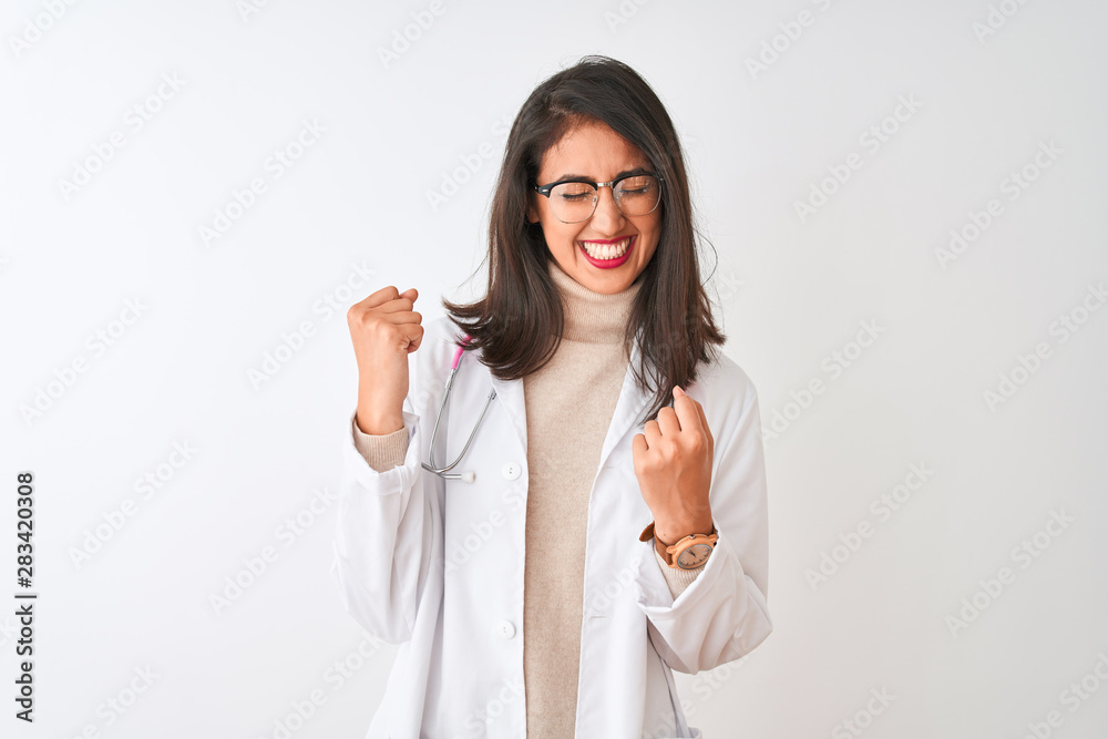 Chinese doctor woman wearing coat and pink stethoscope over isolated white background very happy and excited doing winner gesture with arms raised, smiling and screaming for success. Chinese doctor woman wearing coat and pink stethoscope over isolated white background very happy and excited doing winner gesture with arms raised, smiling and screaming for success.