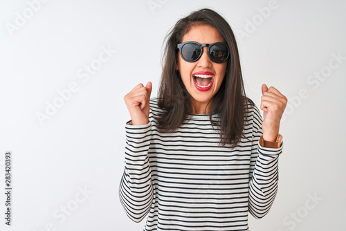 Chinese woman wearing striped t-shirt and sunglasses standing over isolated white background excited for success with arms raised and eyes closed celebrating victory smiling. Winner concept.