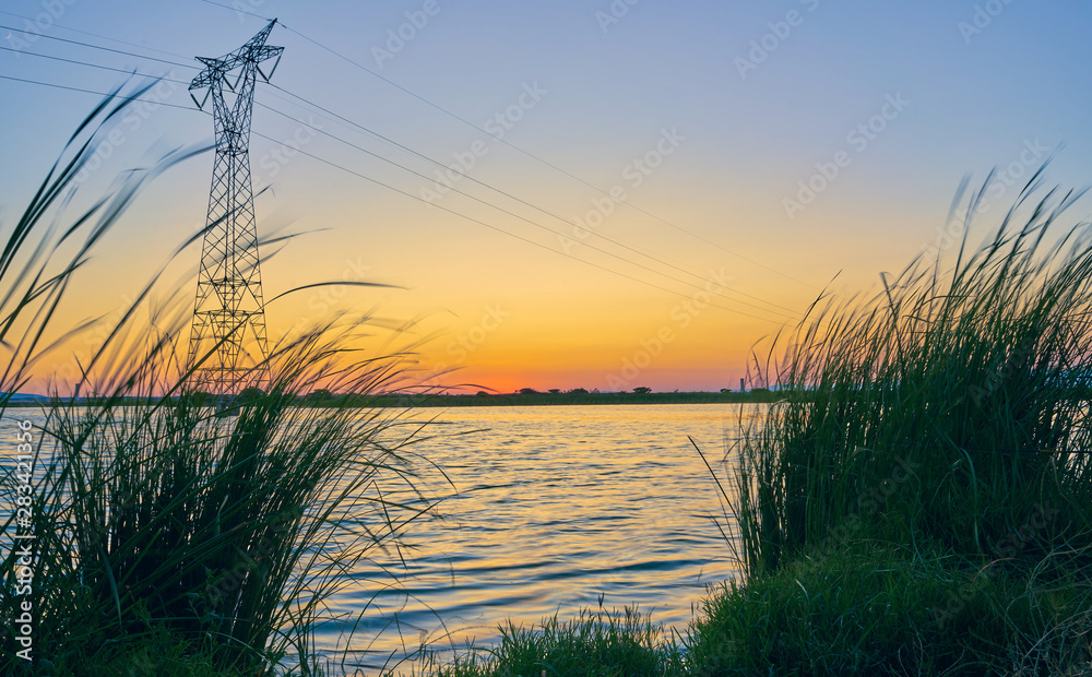 Sunset in a landscape with lake, trees and light towers. Extremadura. Spain