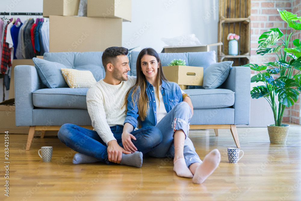 Young beautiful couple sitting on the floor of new apartment, smiling in love happy for moving to a new home Young beautiful couple sitting on the floor of new apartment, smiling in love happy for moving to a new home