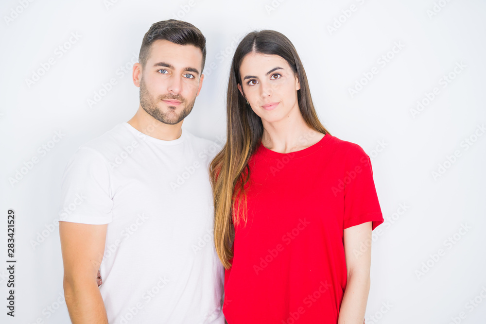 Young beautiful couple together over white isolated background with serious expression on face. Simple and natural looking at the camera. Young beautiful couple together over white isolated background with serious expression on face. Simple and natural looking at the camera.