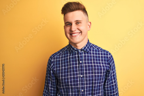 Young handsome man wearing casual shirt standing over isolated yellow background looking away to side with smile on face, natural expression. Laughing confident.