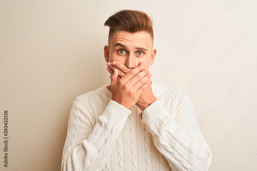 Young handsome man wearing winter sweater standing over isolated white background shocked covering mouth with hands for mistake. Secret concept. Young handsome man wearing winter sweater standing over isolated white background shocked covering mouth with hands for mistake. Secret concept.