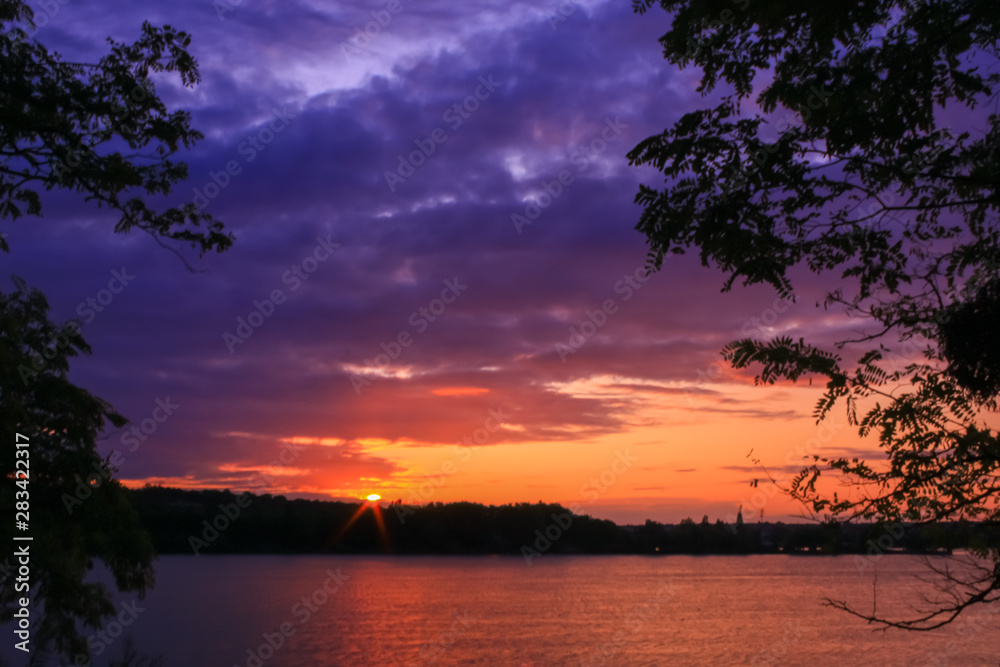 Amazing romantic sunset over the water. Reflection of the colorful sky in the lake. Vegetations in foreground. Amazing romantic sunset over the water. Reflection of the colorful sky in the lake. Vegetations in foreground.