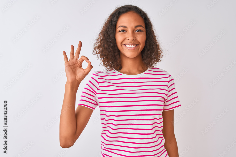 Young brazilian woman wearing pink striped t-shirt standing over isolated white background smiling positive doing ok sign with hand and fingers. Successful expression. Young brazilian woman wearing pink striped t-shirt standing over isolated white background smiling positive doing ok sign with hand and fingers. Successful expression.