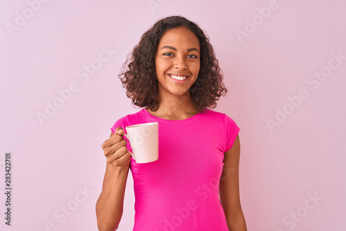 Young brazilian woman drinking cup of coffee standing over isolated pink background with a happy face standing and smiling with a confident smile showing teeth