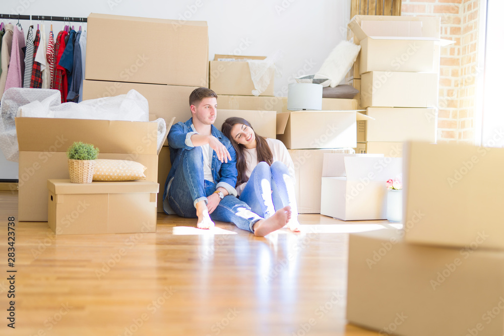 Young beautiful couple relaxing sitting on the floor around cardboard boxes at home, smiling happy moving to a new house Young beautiful couple relaxing sitting on the floor around cardboard boxes at home, smiling happy moving to a new house