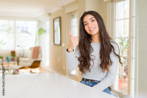 Young beautiful woman at home doing happy thumbs up gesture with hand. Approving expression looking at the camera with showing success.