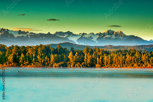 Dramatic light on the Peaks of the Southern Alps behind the forest and Okarito Lagoon photo