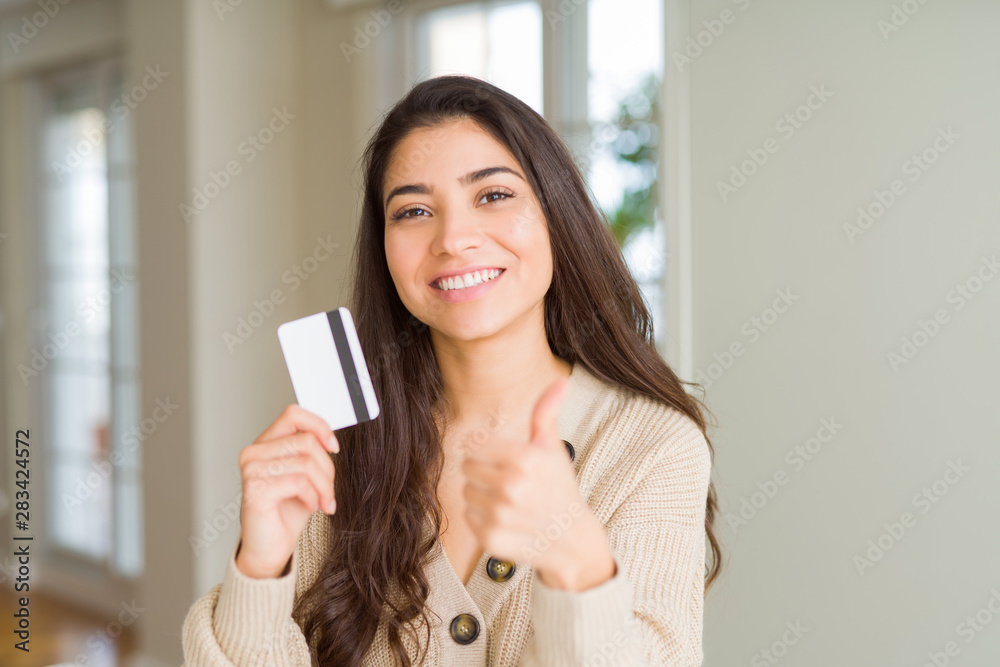Young woman holding credit card as payment happy with big smile doing ok sign, thumb up with fingers, excellent sign Young woman holding credit card as payment happy with big smile doing ok sign, thumb up with fingers, excellent sign
