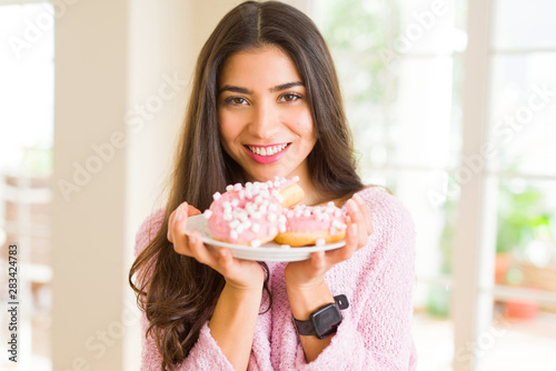 Beautiful young woman smiling holding a plate full of delicious pink donuts