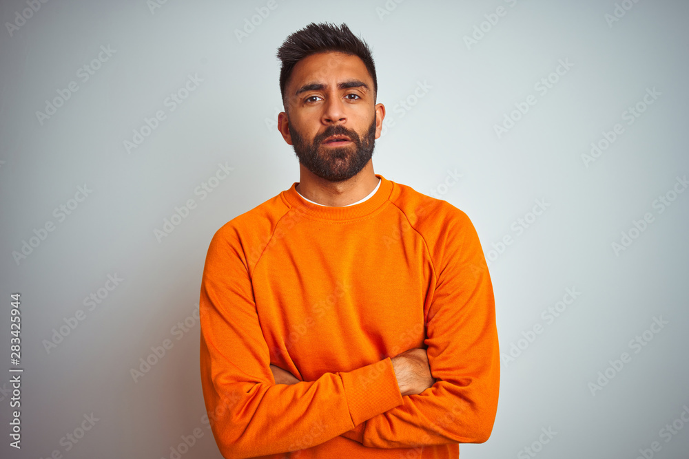 Young indian man wearing orange sweater over isolated white background skeptic and nervous, disapproving expression on face with crossed arms. Negative person.