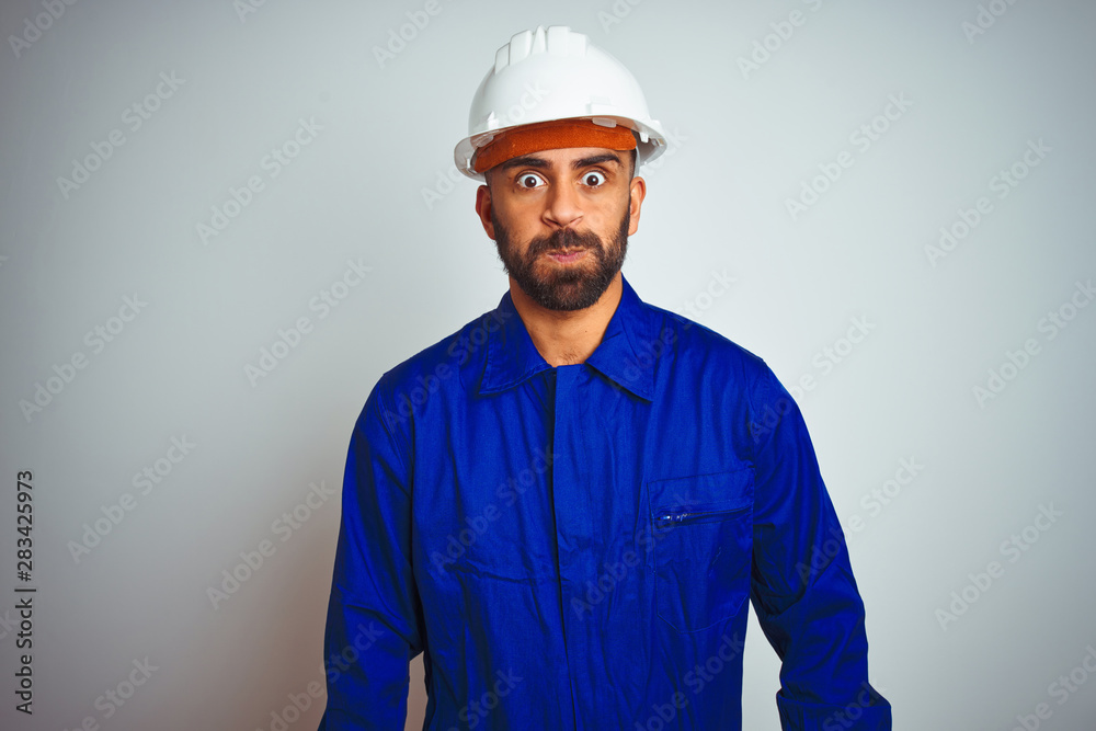 Handsome indian worker man wearing uniform and helmet over isolated white background puffing cheeks with funny face. Mouth inflated with air, crazy expression. Handsome indian worker man wearing uniform and helmet over isolated white background puffing cheeks with funny face. Mouth inflated with air, crazy expression.