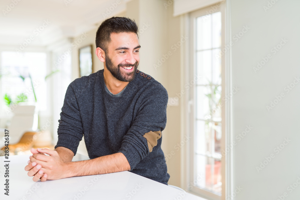 Handsome hispanic man wearing casual sweater at home looking away to side with smile on face, natural expression. Laughing confident. Handsome hispanic man wearing casual sweater at home looking away to side with smile on face, natural expression. Laughing confident.