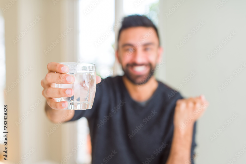 Handsome hispanic man drinking a fresh glass of water screaming proud and celebrating victory and success very excited, cheering emotion Handsome hispanic man drinking a fresh glass of water screaming proud and celebrating victory and success very excited, cheering emotion