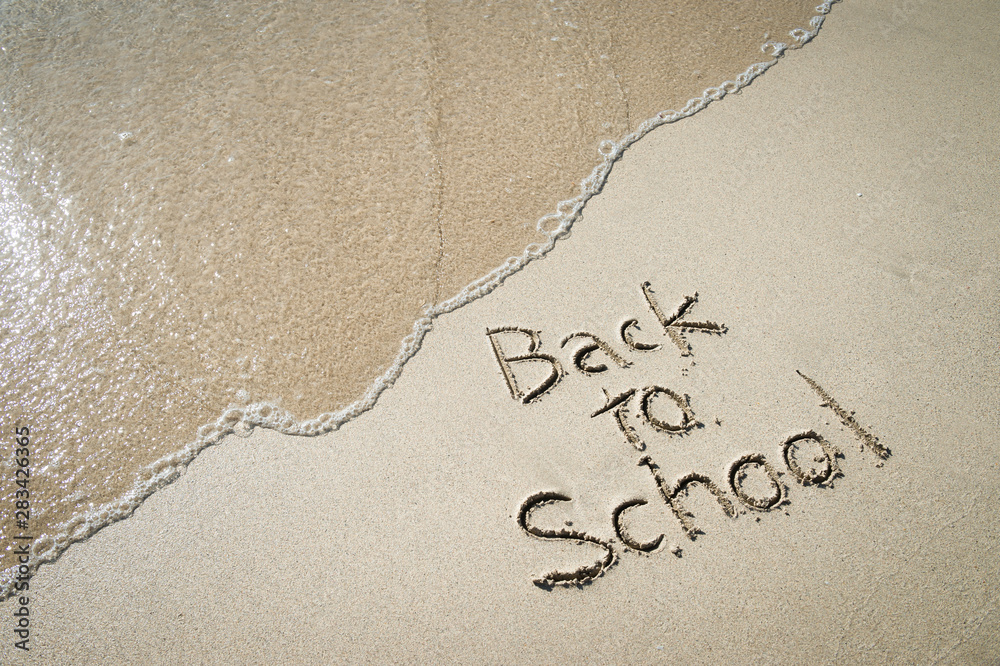 Fototapeta premium Back to School message handwritten on smooth sand beach with incoming wave