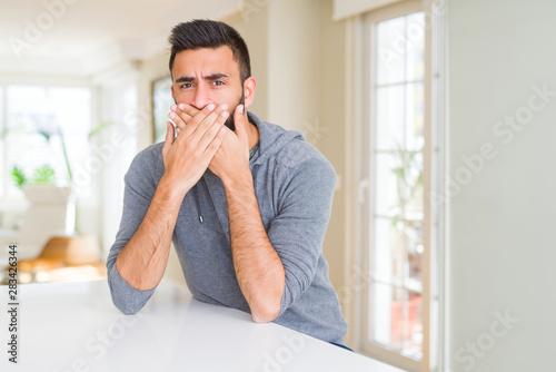 Handsome hispanic man wearing casual sweatshirt at home shocked covering mouth with hands for mistake. Secret concept.