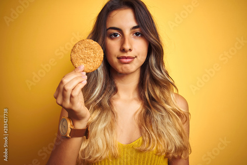 Young beautiful woman eating biscuit over grey isolated background with a confident expression on smart face thinking serious