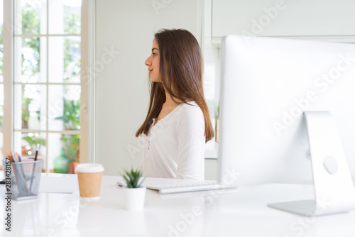 Beautiful young woman working using computer looking to side, relax profile pose with natural face with confident smile.