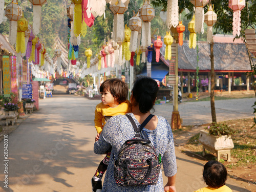 Asian woman carrying and taking her baby girls to visit a Buddhist temple - travel helps ignite children's imagination and encourages them to embrace their new experiences during their childhood © OleCNX