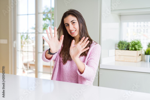 Beautiful young woman wearing pink sweater afraid and terrified with fear expression stop gesture with hands, shouting in shock. Panic concept.