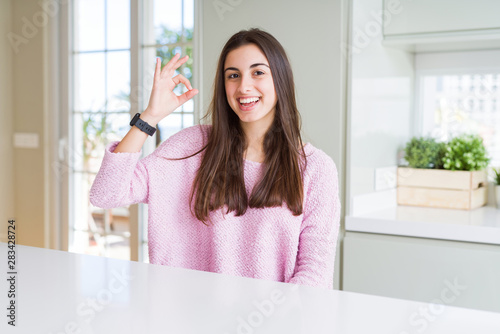 Beautiful young woman wearing pink sweater smiling positive doing ok sign with hand and fingers. Successful expression. © Krakenimages.com