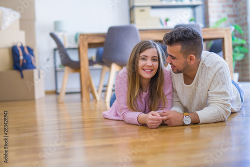 Young beautiful couple in love moving to new home, lying on the floor around cardboard boxes, very happy and cheerful for new apartment