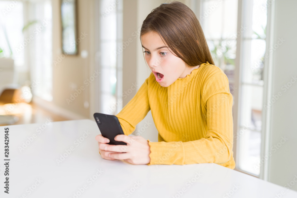 Beautiful young girl kid sending a message using smartphone scared in shock with a surprise face, afraid and excited with fear expression Beautiful young girl kid sending a message using smartphone scared in shock with a surprise face, afraid and excited with fear expression