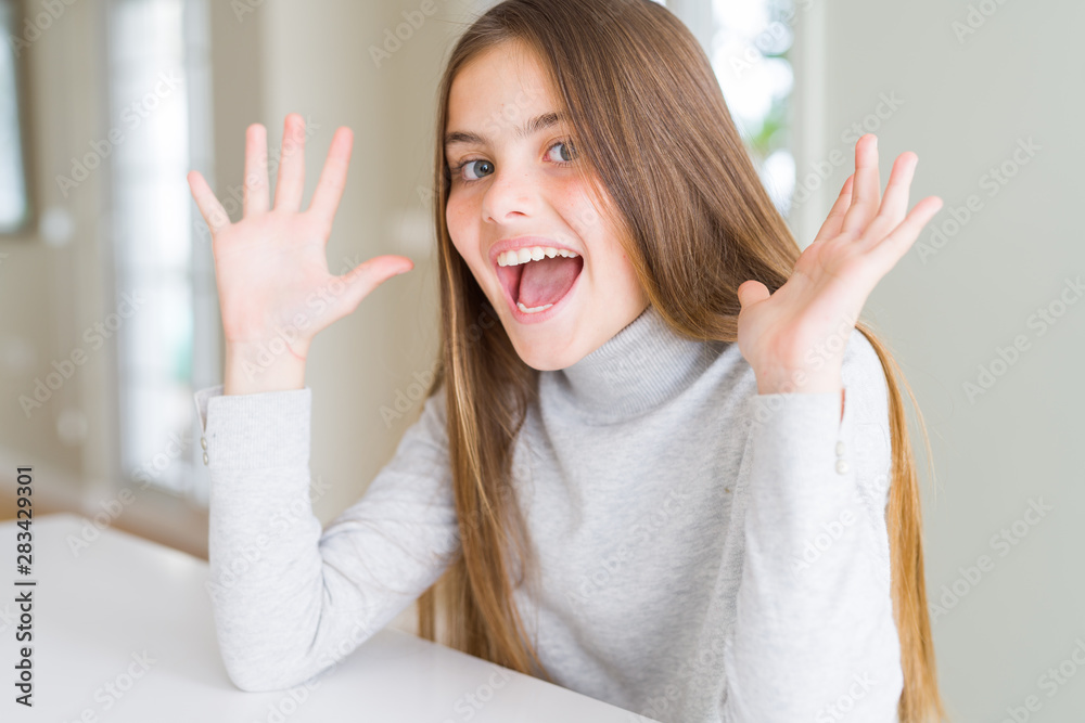 Beautiful young girl kid wearing turtleneck sweater celebrating crazy and amazed for success with arms raised and open eyes screaming excited. Winner concept Beautiful young girl kid wearing turtleneck sweater celebrating crazy and amazed for success with arms raised and open eyes screaming excited. Winner concept