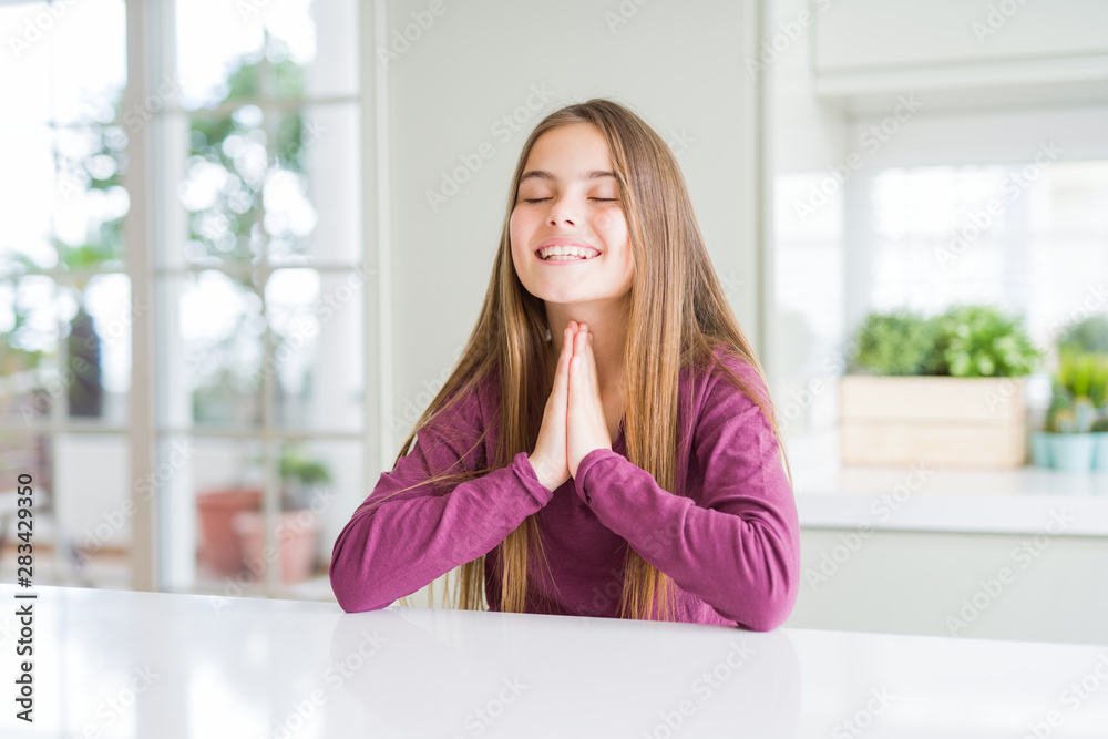 Beautiful young girl kid on white table praying with hands together asking for forgiveness smiling confident. Beautiful young girl kid on white table praying with hands together asking for forgiveness smiling confident.