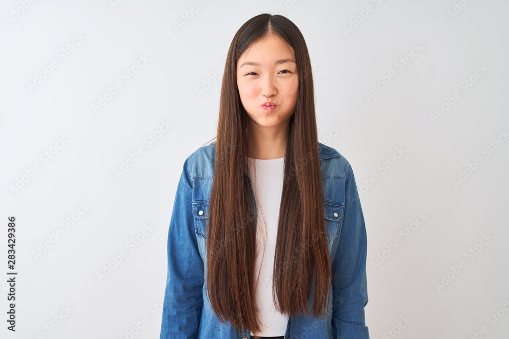 Young chinese woman wearing denim shirt standing over isolated white background puffing cheeks with funny face. Mouth inflated with air, crazy expression. Young chinese woman wearing denim shirt standing over isolated white background puffing cheeks with funny face. Mouth inflated with air, crazy expression.