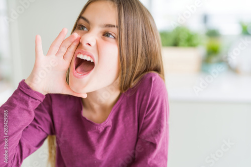 Beautiful young girl kid shouting and screaming loud to side with hand on mouth. Communication concept.