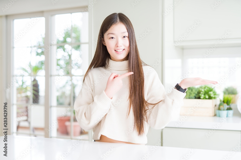 Beautiful Asian woman wearing casual sweater amazed and smiling to the camera while presenting with hand and pointing with finger. Beautiful Asian woman wearing casual sweater amazed and smiling to the camera while presenting with hand and pointing with finger.
