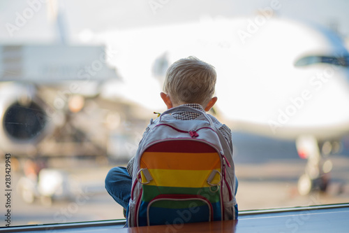 Tablou pe pânză Young boy sitting looking out of the window at the airport anxiously waiting for