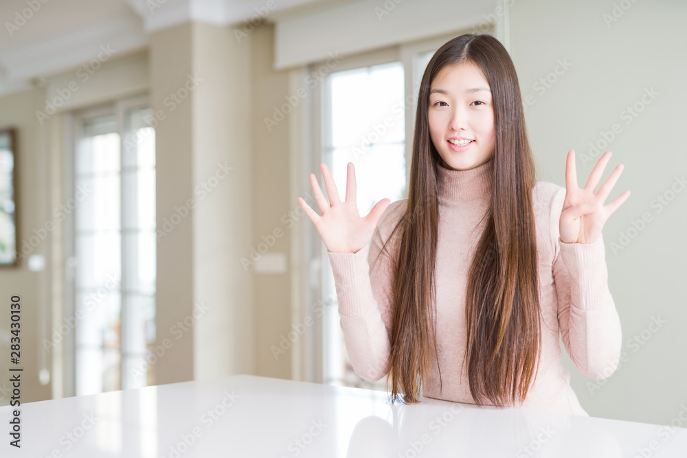 Beautiful Asian woman wearing casual sweater on white table showing and pointing up with fingers number nine while smiling confident and happy. Beautiful Asian woman wearing casual sweater on white table showing and pointing up with fingers number nine while smiling confident and happy.
