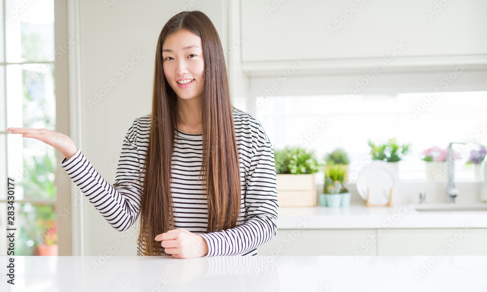 Beautiful Asian woman wearing stripes sweater smiling cheerful presenting and pointing with palm of hand looking at the camera. Beautiful Asian woman wearing stripes sweater smiling cheerful presenting and pointing with palm of hand looking at the camera.