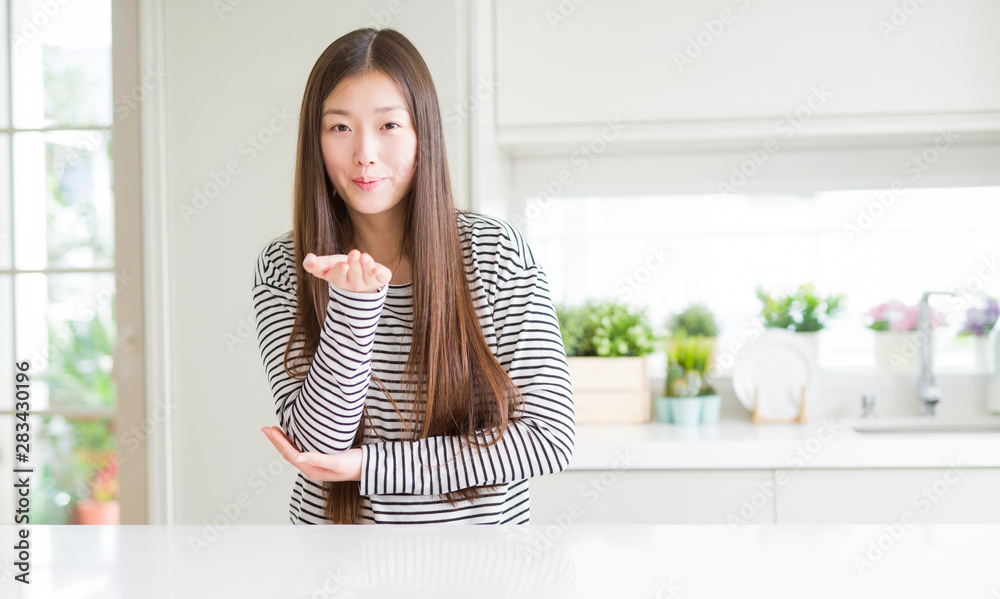 Beautiful Asian woman wearing stripes sweater looking at the camera blowing a kiss with hand on air being lovely and sexy. Love expression. Beautiful Asian woman wearing stripes sweater looking at the camera blowing a kiss with hand on air being lovely and sexy. Love expression.