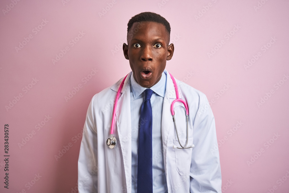 African american doctor man wearing stethoscope standing over isolated pink background afraid and shocked with surprise expression, fear and excited face. African american doctor man wearing stethoscope standing over isolated pink background afraid and shocked with surprise expression, fear and excited face.