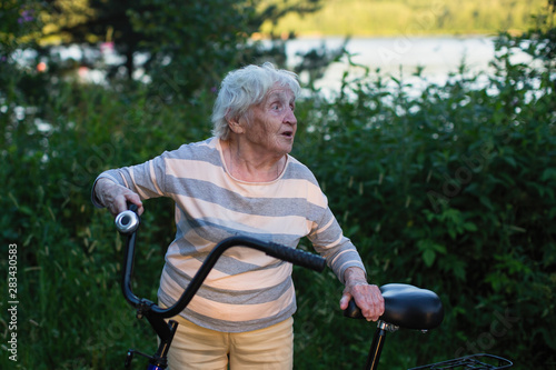 Elderly woman with bike an outdoor. Pensioner's bicycle ride. © De Visu