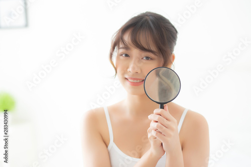 Beautiful young asian woman happy with magnifying skin of acne, beauty asia girl smiling check skincare of face, female analyzing trouble, cosmetic and makeup, health care and wellness concept.