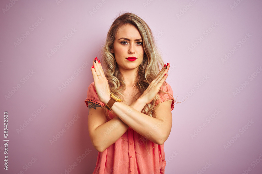Young beautiful woman wearing t-shirt standing over pink isolated background Rejection expression crossing arms doing negative sign, angry face